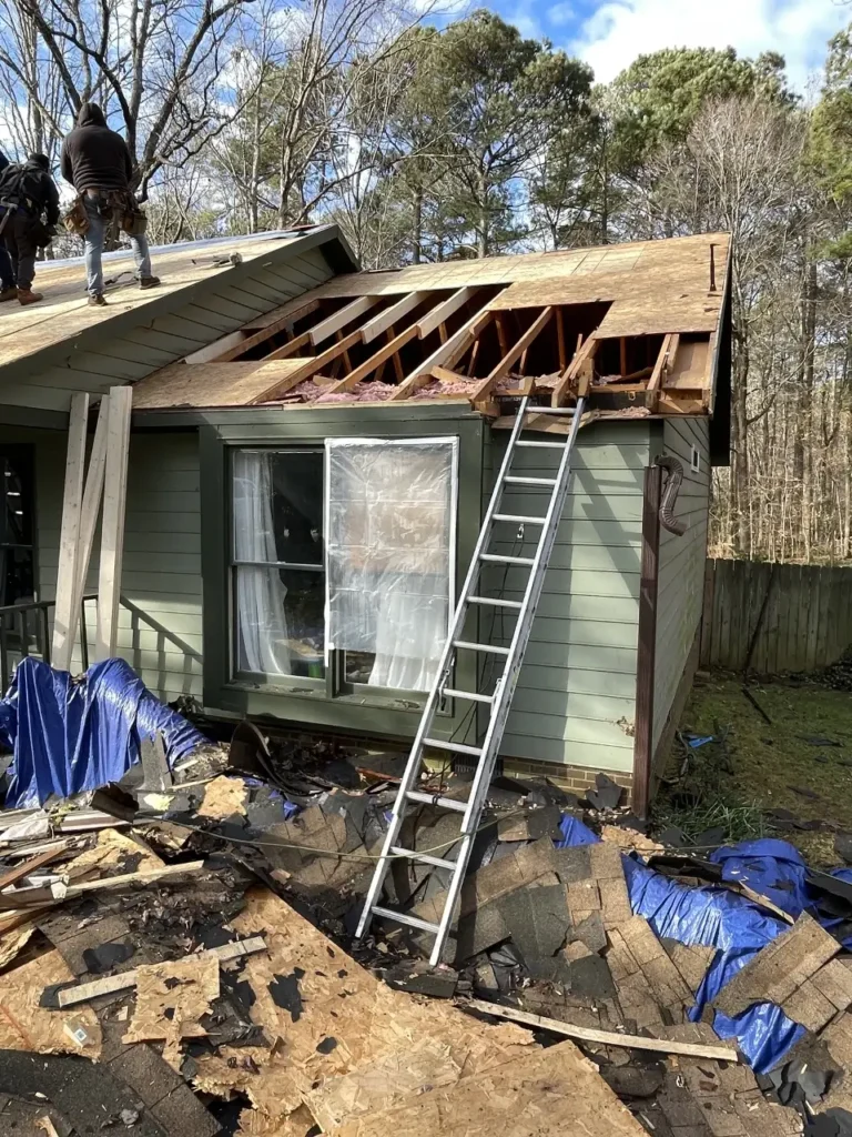 image of a damaged house with a ladder attached to side and roofers on the roof